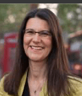 headshot of Ute Stephan, a brown-haired woman smiling at the camera. The background is a blurred cityscape. 
