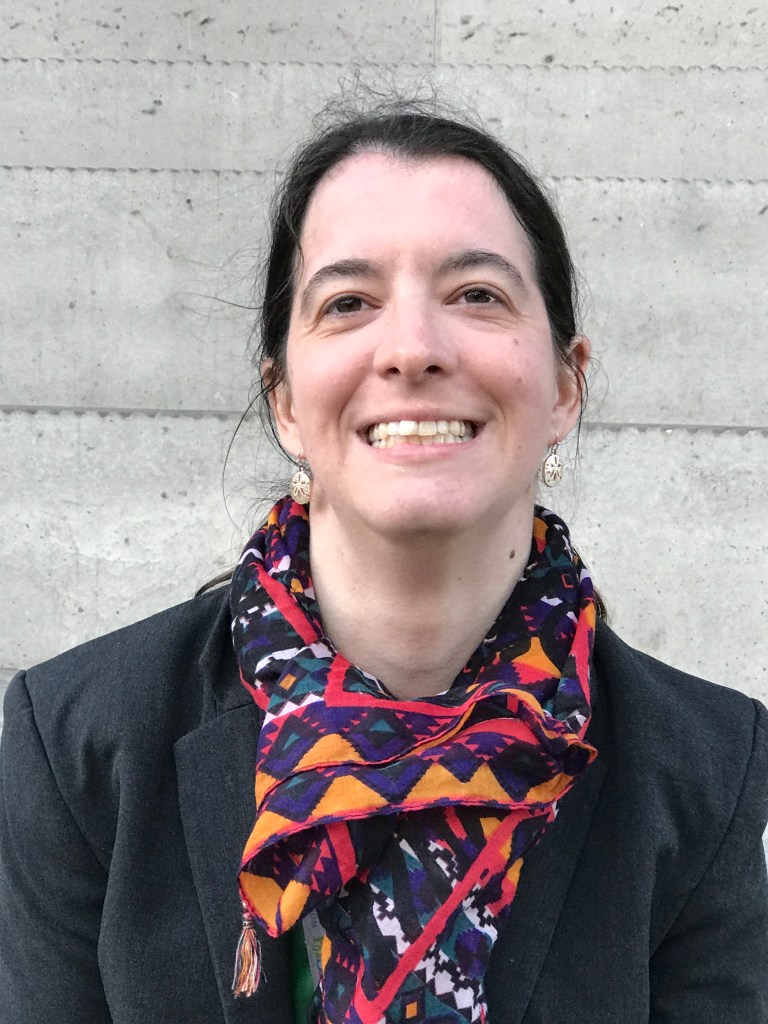 headshot of Terry-Lynn Langdon wearing a black top and a colourful scarf, standing in front of a grey brick wall