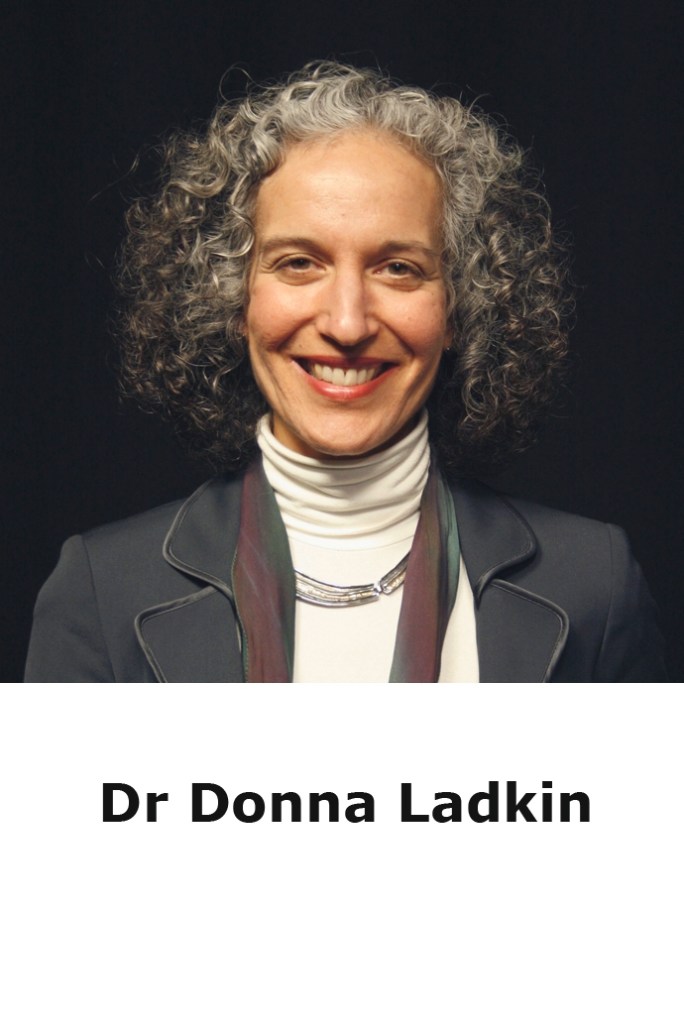 head shot of Donna Ladkin smiling to the camera. She has curley hair and wears a black jacket with a light top. She stands in front of a black background