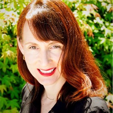 headshot of Marieshka Barton who has red hair and wears a black top. She stands in front of a tree