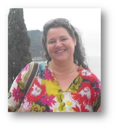 Head shot of Carmen Svastics. She is wearing a colourful top and stands in front of scenic background. 