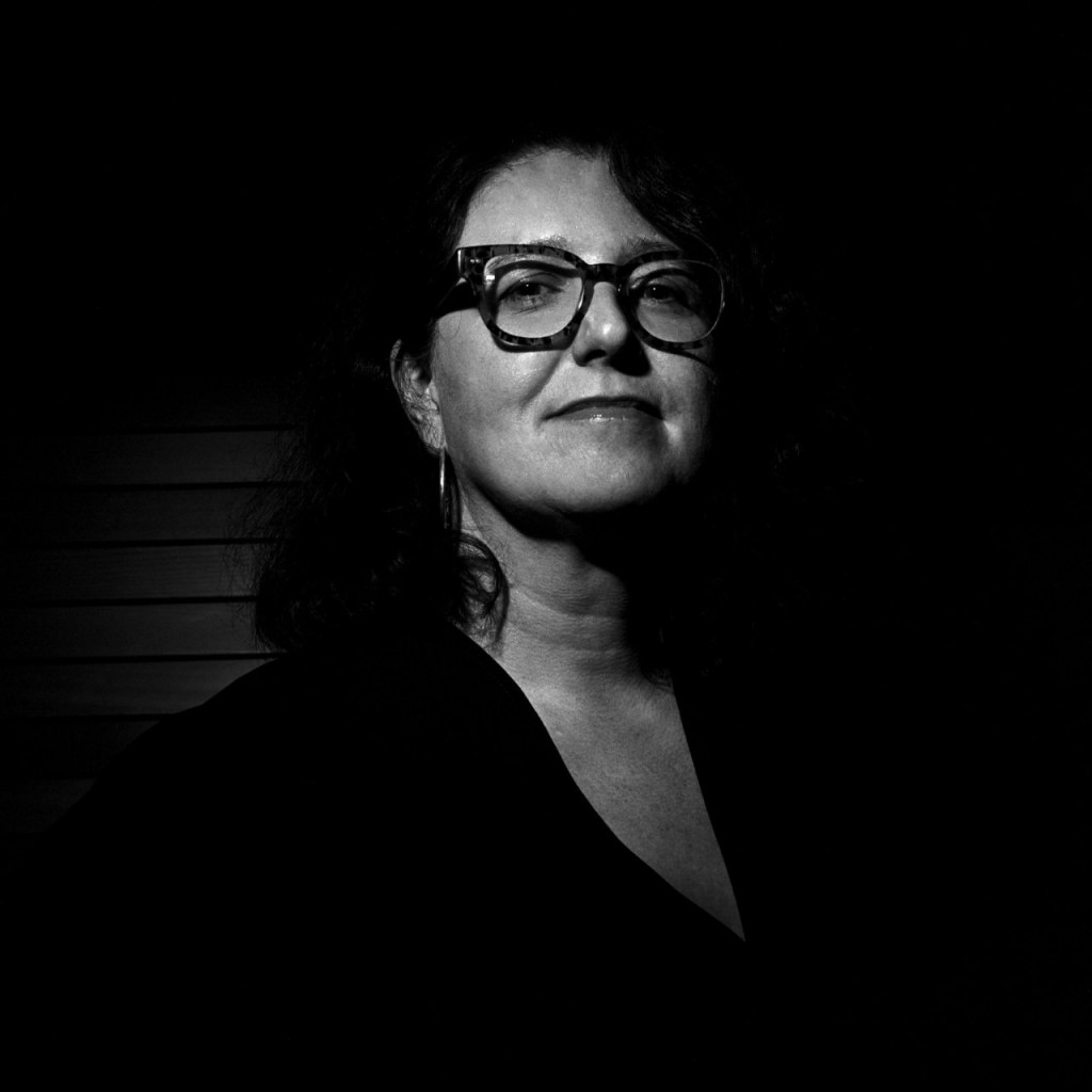 back and white photo of Alison Pullen wearing a dark top in front of a dark background. 