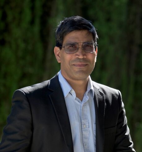 upper body shot of Israr Qureshi, a South Asian man wearing a jacket, a dress shirt and glasses