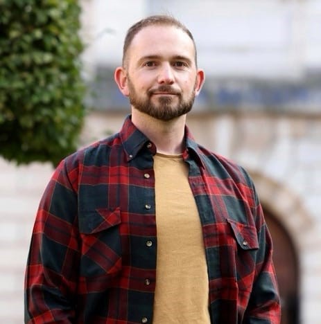 upper body shot of Lee Wainwright wearing academic robes. He has short hair and a beard.