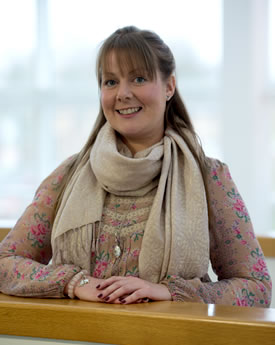 Upper body shot of Leighanne Higgins, a white woman with red hair wearing beige coloured wooly top