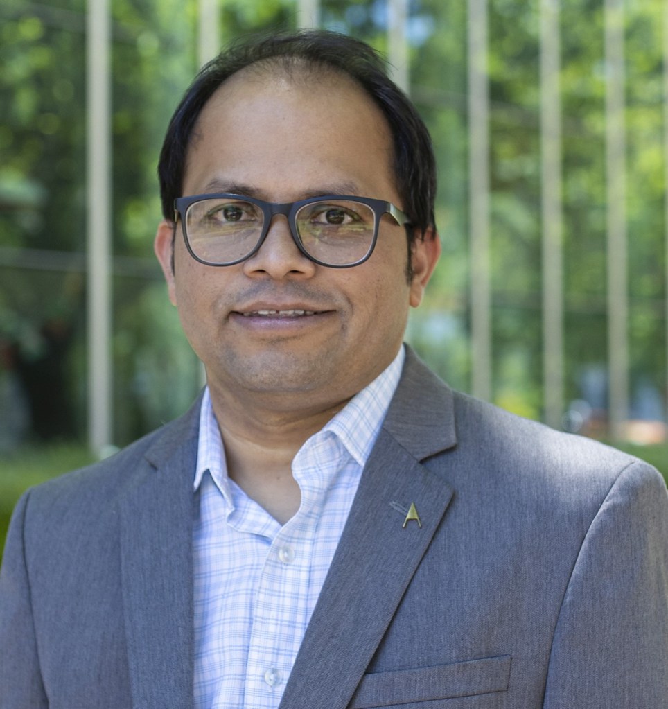 Head shot of Pradeep Hota , an Indian man wearing glasses and a blue suit jackedt over a white shirt