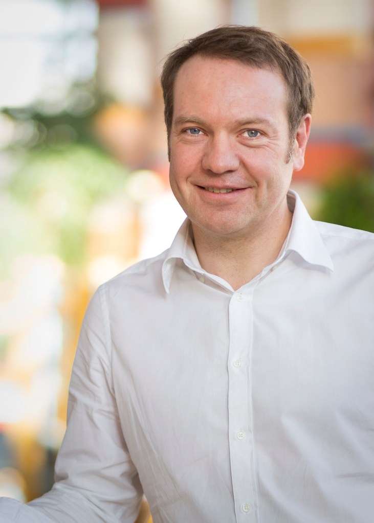 Upper body shot of Paul Tracey, a white man wearing a white shirt in front of a blurred background