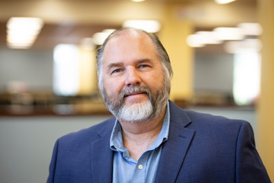 photo of Eduardo Millet, a middle-aged man with a grey beard wearing a dress shirt and jacket in front of a blurred background of a building