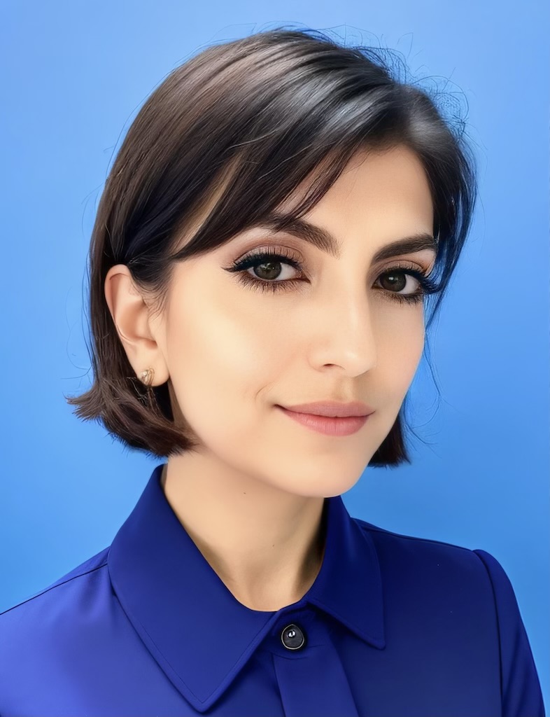 Headshot of Ren Lovegood. They have short dark hair and are in front of a blue background smiling at the camera