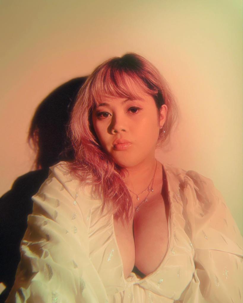 headshot of Dani Waldo , a Canadian Phillipino woman with long blonde hair wearing a blush topic and a sparkly neckless