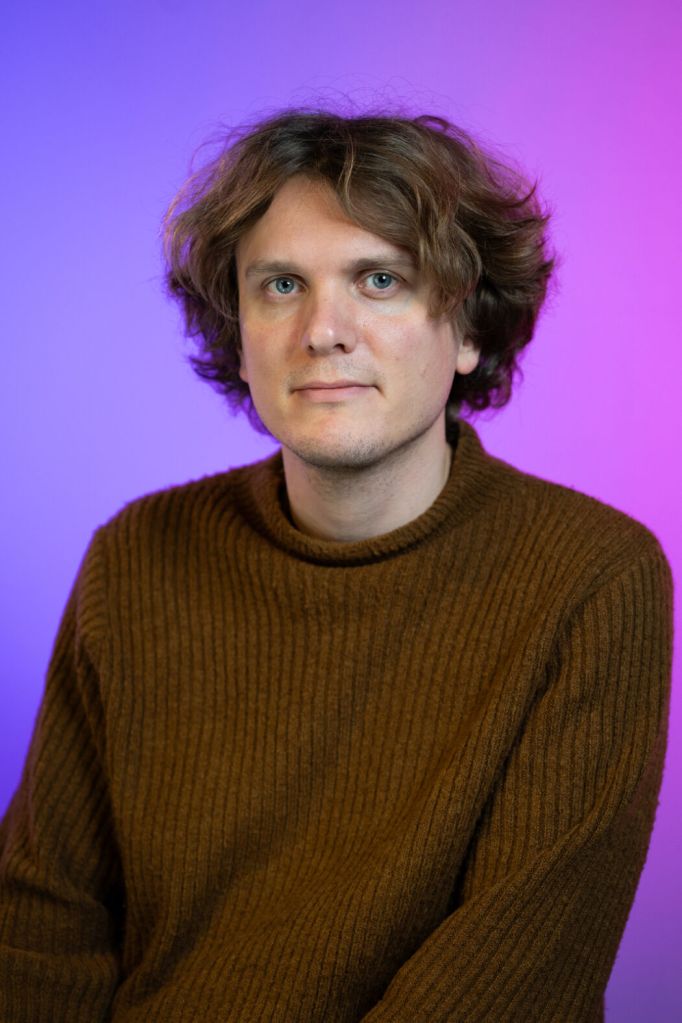 headshot of Jonatan Södergren, a man with tufty black hair wearing a black top in front of a purple background