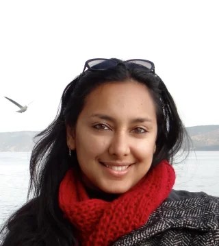 head shot of Prarthana Purkayastha, an Indian woman with long dark hair , sunglasses on her head and a red scarf warped around her neck