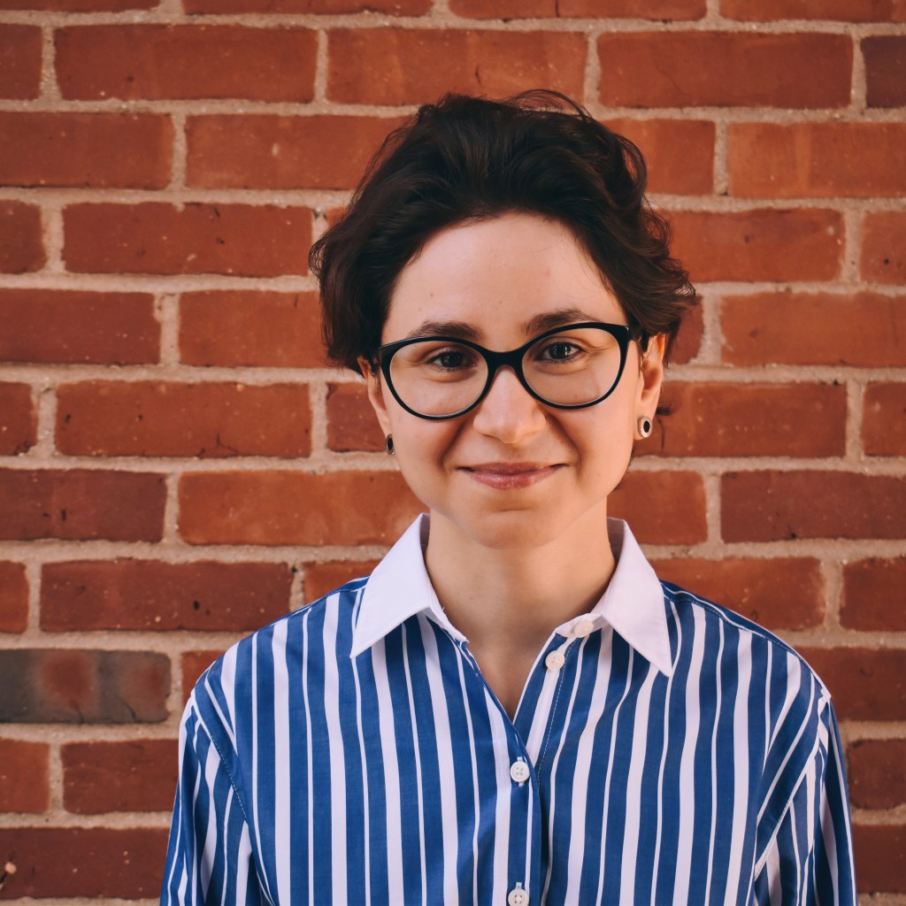 headshot of Elena Elkanova, a person with short black hair wearing glasses