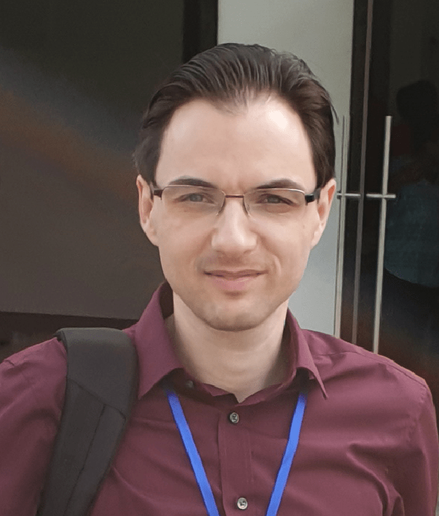 Head shot of Catalin Brylla, a light skinned man with dark brown hair and glasses. Hewears a maroon shirt and a bright blue lanyard. he smiles broadly at the camera