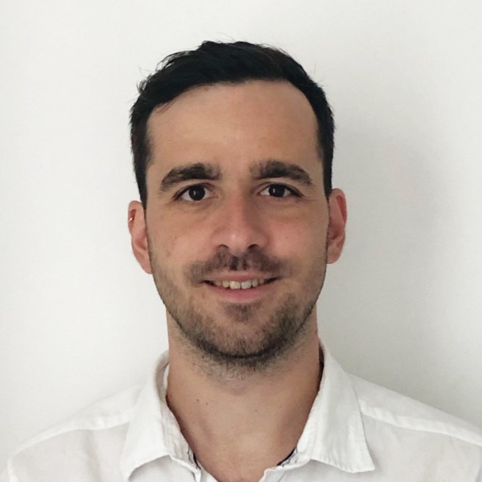 headshot of Oguzhan Okumus who has short dark hair, a moustache and a light beard  wearing a white shirt and is in front of a white backdrop