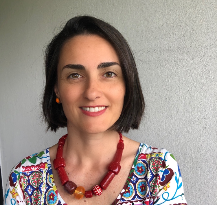 Headshot of Daniela Bozani ey who has medium-length dark hair. She wars a colourful top and is in front of a grey background
