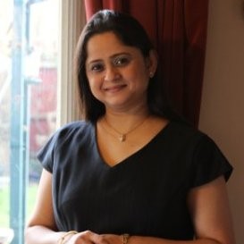upper body photo of Manjiri who is an Indian women with medium length dark hair. she stands near a window