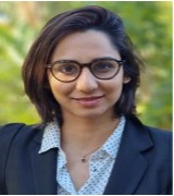 head shot of Adiilah Boodhoo who has short dark hair. She wars glasses a shirt and dark jacket