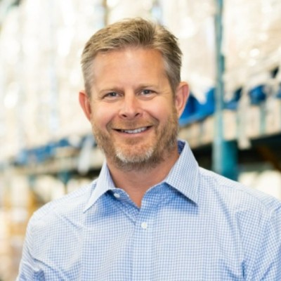 headshot of Neil who has light skin and blonde hair and a short beard. He wears a blue shirt and smiles broadly