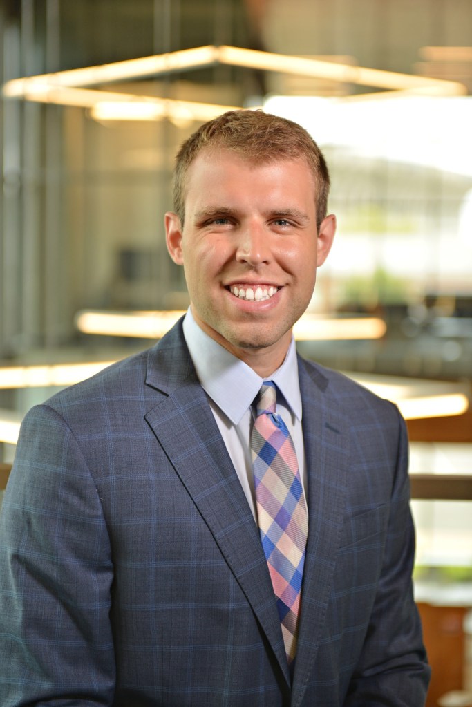 upper body shot of Wyatt who has very short dark hair and wears a grey jacket and blue and grey patterned tie.