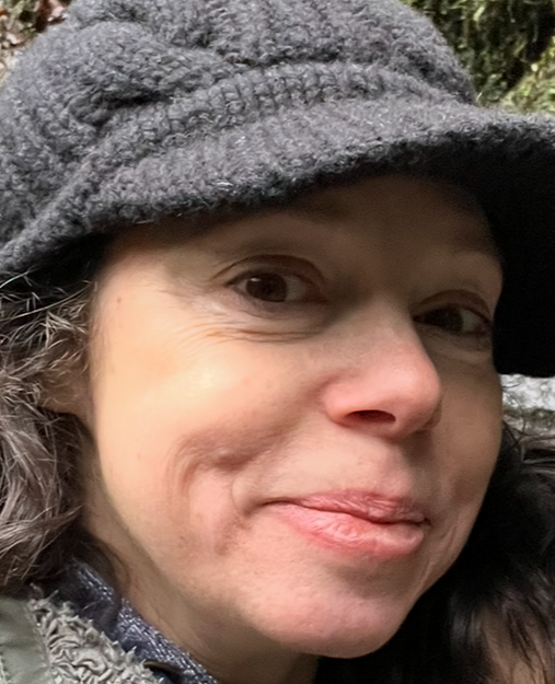 close up head shot of Melea who has light skin. Her face is partly covered by a grey hat. 