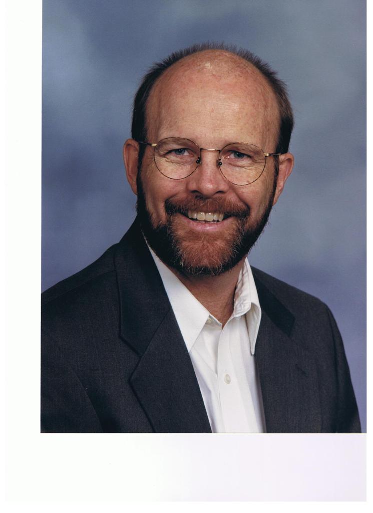 head shot of Blaine a white man with a beard and very short hair. He are a black jacket and a white shirt. 