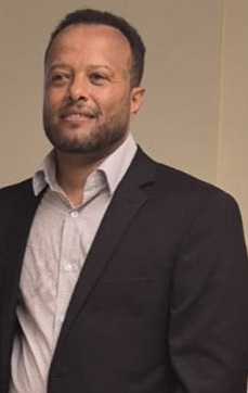 Photo of Abebe, a black man with short hair wearing a dress shirt and jacket