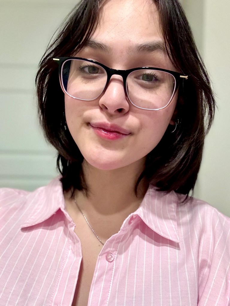 eadshot of Eunice Tunggal. She is a woman with light skin, dark brown hair, and light brown eyes. She wears a pink and white striped collared shirt and black glasses. The background is a white wall.