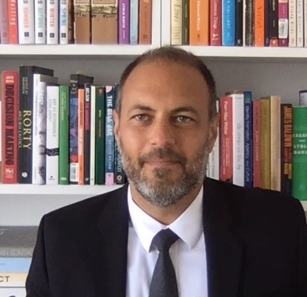 Headshot of man in jacket and tie in front of bookshelf