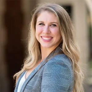 Headshot of Ashley a light skinned woman with long blonde hair. she stands slightly at an angle looking at the camera. She wars a blue blazer 