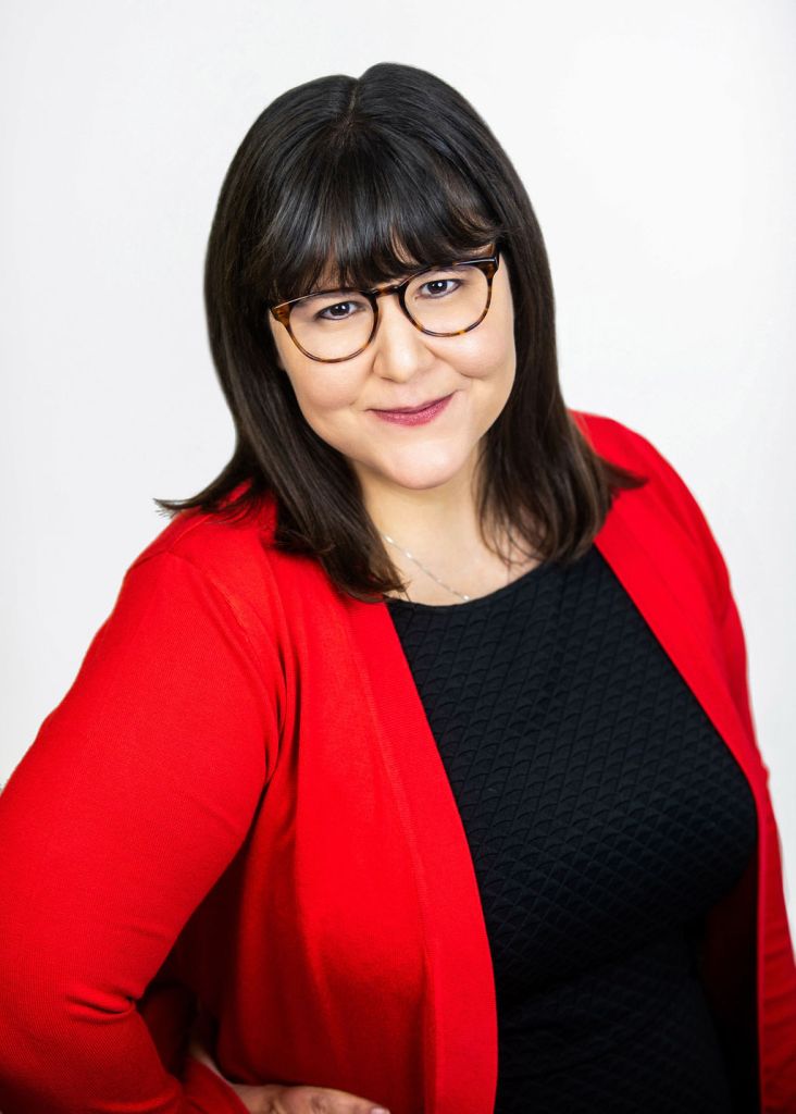 Woman with brown hair and glasses smiling and wearing red bright red sweater