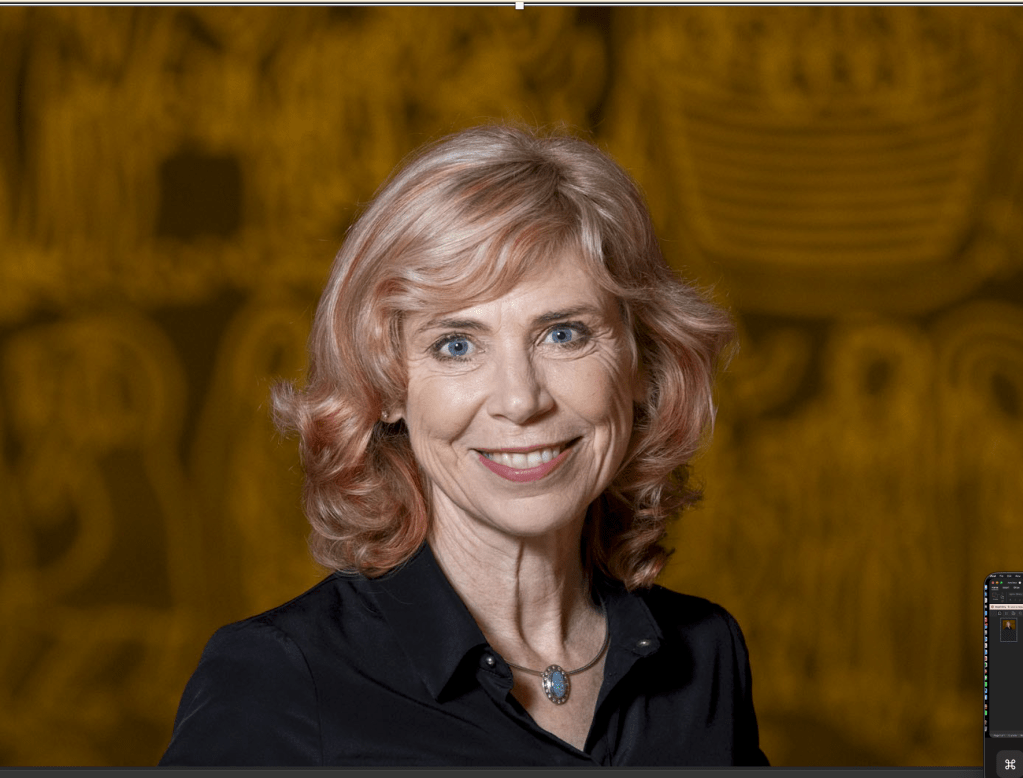 Photograph of Susi Geiger with shoulder-length wavy blonde hair wearing a black shirt and a pendant necklace. 